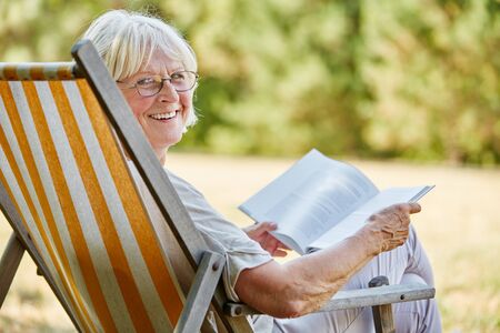Old happy lady reading a book and smiling in summer in the natureの写真素材