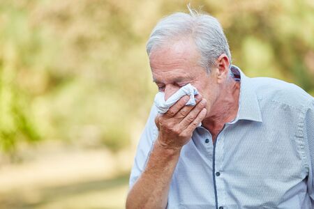 Old man with a cold using a tissue in the natureの写真素材