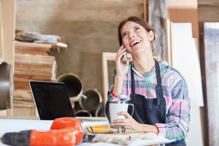 Woman at workshop calling on the phone and laughingの写真素材