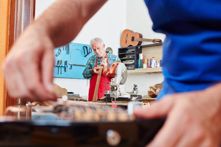 Luthier repairing guitar while collegue repairs electric guitar