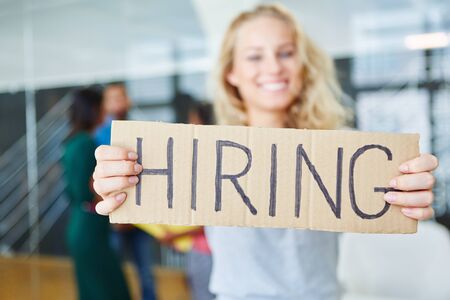 Blond woman holding sign with word "hiring" at start-up companyの写真素材