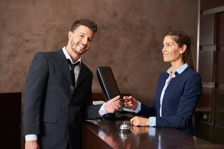 Smiling guest paying with his credit card at hotel receptionの写真素材