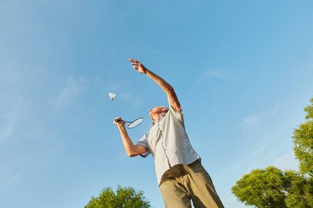 Old man making a service while playing badminton in summerの写真素材