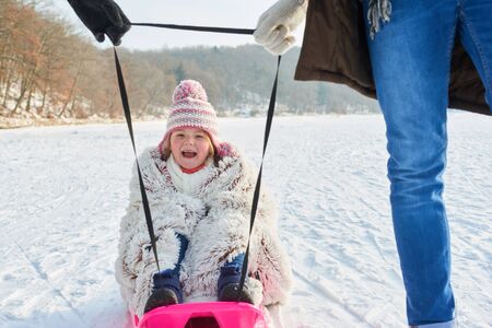 Child laughing and having fun while sledding with her family in winter