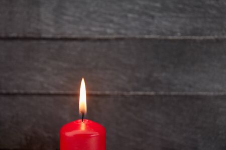 Burning red candle with flame makes candlelight on wooden background