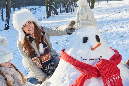 Mother and daughter in winter building a snowman together