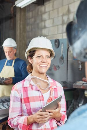 Young woman as metalworker apprentice with laptop in metallurgy factoryの写真素材