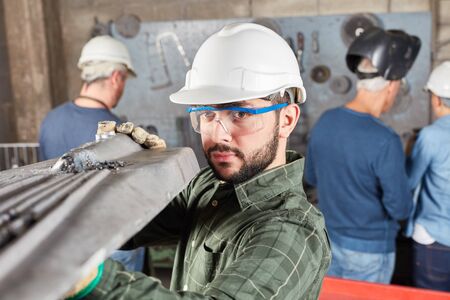 Quality control in metallurgy factory with worker carrying metal workpiece