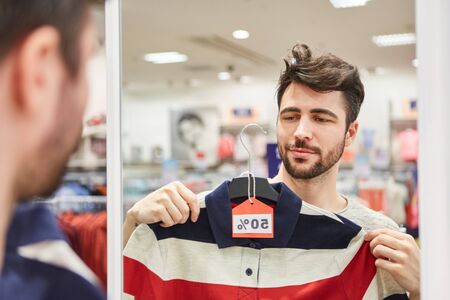 Young man in shirt buying in front of the mirror while trying on in fashion businessの写真素材