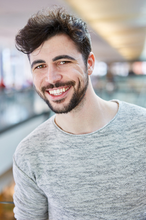 Happy young man with beard and gray shirt in shopping mallの写真素材