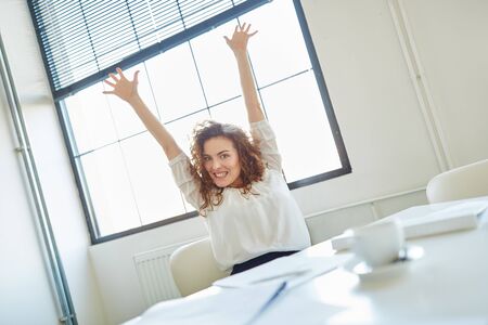 Woman in office celebrating her success with streched arms and handsの写真素材