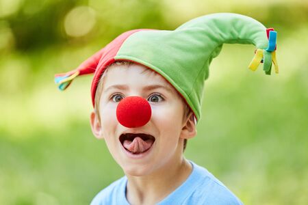 Boy with red nose and fool's cap in the carnival sticks out his tongueの写真素材