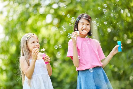 Two girls are happy about the floating soap bubbles in nature