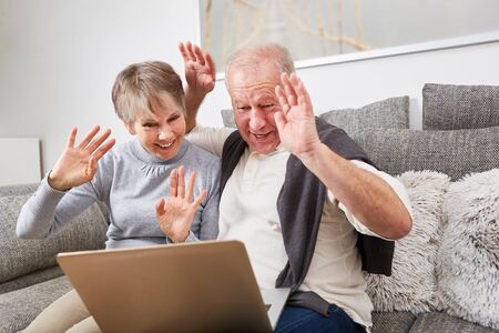 Senior couple wave at computer while video chatting with laptop