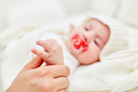 Adult lovingly holds an infant's little hand with pacifierの写真素材