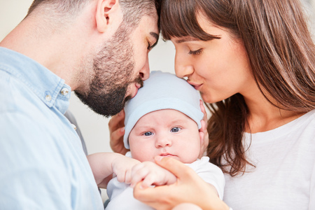 Mother and father together kiss their baby on the forehead