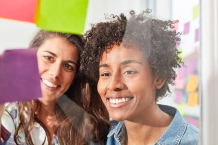 Two young women in a multicultural start-up team brainstorming togetherの写真素材