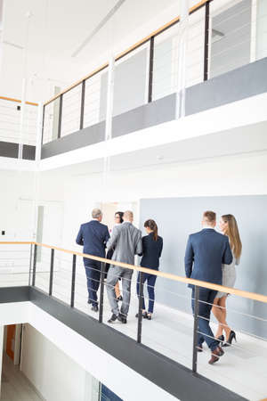 Full length of business people walking by railing on corridor in office