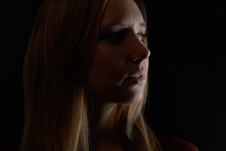 Pensive young blond woman looks to the side in the darkの写真素材