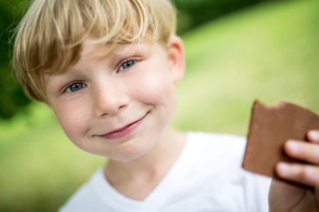 Happy boy eating chocolate cookie in summerの写真素材