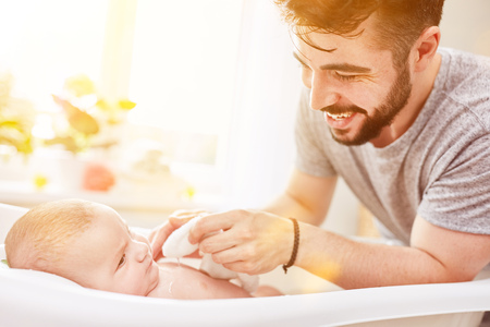 Father bathes baby in baby bath during his parental leave