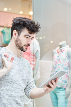 Young man as a customer with tablet computer in front of a fashion storeの写真素材