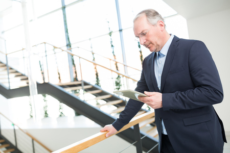Senior businessman using tablet computer while leaning on railing in officeの写真素材