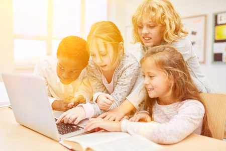 Group of kids is sitting in front of a laptop computer in the elementary school