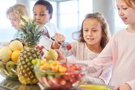 Children at the canteen cafeteria in kindergarten or elementary school pick up fruitの写真素材
