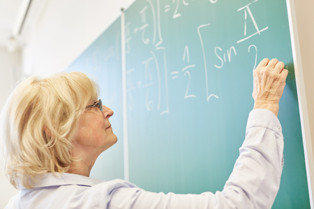 Senior woman as math university teacher writes on chalkboardの写真素材