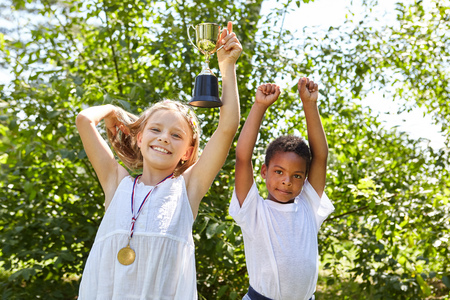Children as multicultural team cheer together with winner cup and medalの写真素材