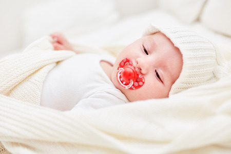 Baby with cap and pacifier lying relaxed on his back at home