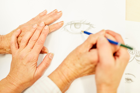 Senior does a drawing in painting therapy and is supported by therapist