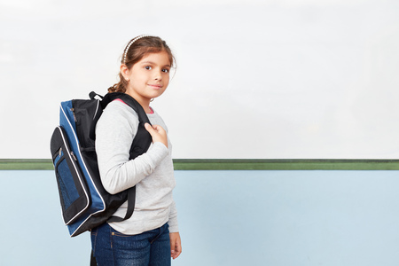 Happy girl as a school-boy with satchels in a school in front of the whiteboard