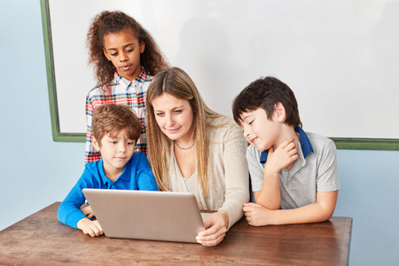 Teacher and elementary school students learn together at the laptop computerの写真素材