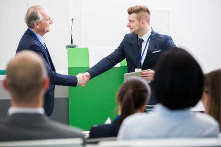 Confident male professional shaking hands with colleague in lecture hallの写真素材