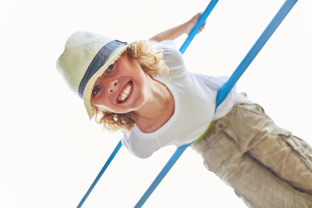 Sporty boy is doing gymnastics on a climbing pole on a playground