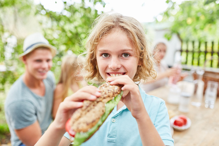Blond boy is eating a fresh baguette while having breakfast in the gardenの写真素材
