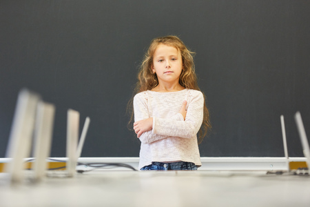 Girl as a student stands with crossed arms in elementary school at the blackboardの写真素材