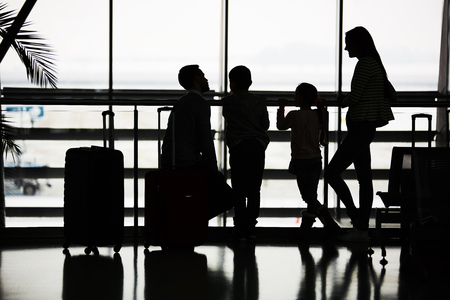Family waits for flight on family vacation at stopover in airport terminalの写真素材
