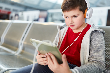 Boy with headphone and tablet listens to music in wait before the flight in the airportの写真素材