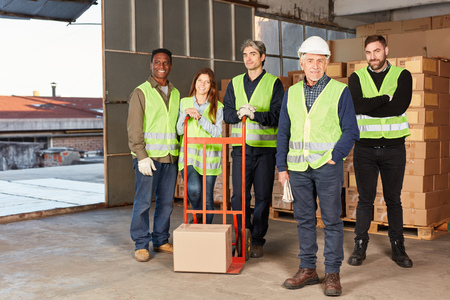 Group of workers as a logistics team with handcart and package in a warehouse