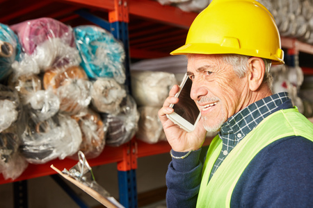Senior as warehouse worker with clipboard talking on mobile phone in carpet storeの写真素材