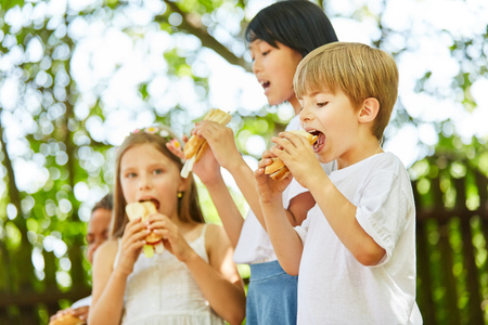 Group of kids at a party eat delicious baguette rolls togetherの写真素材