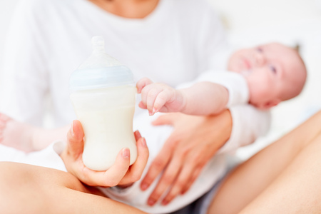 Mother holds baby baby bottle for feeding her babyの写真素材