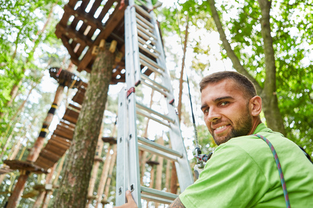 Young man stands in front of the ladder in the high ropes course at the teambuilding eventの写真素材
