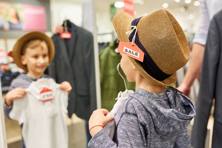 Boy in hat shop in front of the mirror in fashion store during sale actionの写真素材