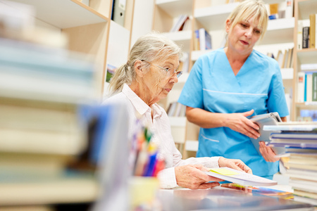 A senior citizen educates herself and is cared for by a nurse in the libraryの写真素材