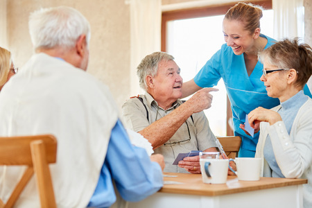 Nursing lady has fun with a group of seniors playing cards in the nursing home