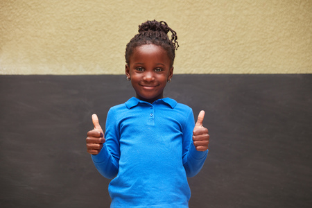 African girl in front of a blackboard holds both thumbs up as a sign of successの写真素材